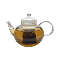 Teekanne aus Glas mit flüssigem Mango Maracuja Grüntee und losen Grünteeblättern